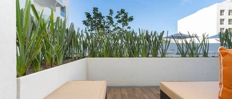 Een balkon met twee beige zithoeken, een houten vloer en uitzicht op gebouwen en groen.