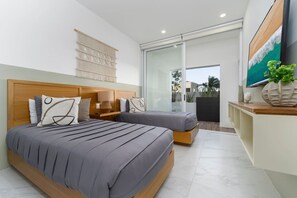 A modern bedroom with a large bed, a smaller bed, a nightstand, a lamp, a wall-mounted TV, and a sliding glass door leading to an outdoor area. - Heart of Cabo|3BR Oasis|Rooftop Spa|Poolside (Cabo San Lucas)