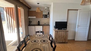 A dining area with a wooden table and chairs, a kitchen with appliances, and a television. - Apartment for 6 people at the base of the slopes: L'Ecrin des Neiges (Chamrousse)