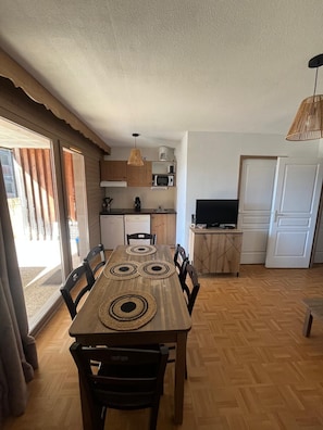 A dining area with a wooden table and chairs, a kitchen with appliances, and a television. - Apartment for 6 people at the base of the slopes: L'Ecrin des Neiges (Chamrousse)