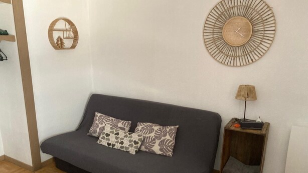 A living room with a grey sofa, patterned cushions, a wooden side table with a lamp, and a wall clock. - Apartment for 6 people at the base of the slopes: L'Ecrin des Neiges (Chamrousse)