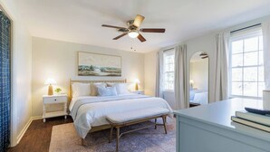 A bedroom with a bed, bedside tables, a ceiling fan, a large window with curtains, and a rug. - Huge Luxury Home | Game Room + Fenced Yard (Valdosta)