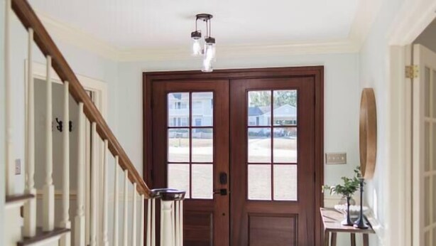 A hallway with a wooden staircase, a dark wooden door, and a light-colored floor. - Huge Luxury Home | Game Room + Fenced Yard (Valdosta)