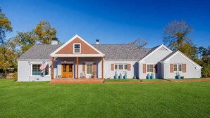 A two-story house with a front porch, a flag, and a well-maintained lawn. - Huge Luxury Home | Game Room + Fenced Yard (Valdosta)