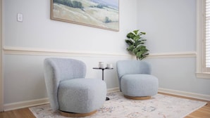 A room with two grey armchairs, a small table with a cup, a plant, and a painting on the wall. - Huge Luxury Home | Game Room + Fenced Yard (Valdosta)