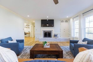 A living room with a fireplace, two sofas, a coffee table, and a TV mounted above the fireplace. - Huge Luxury Home | Game Room + Fenced Yard (Valdosta)