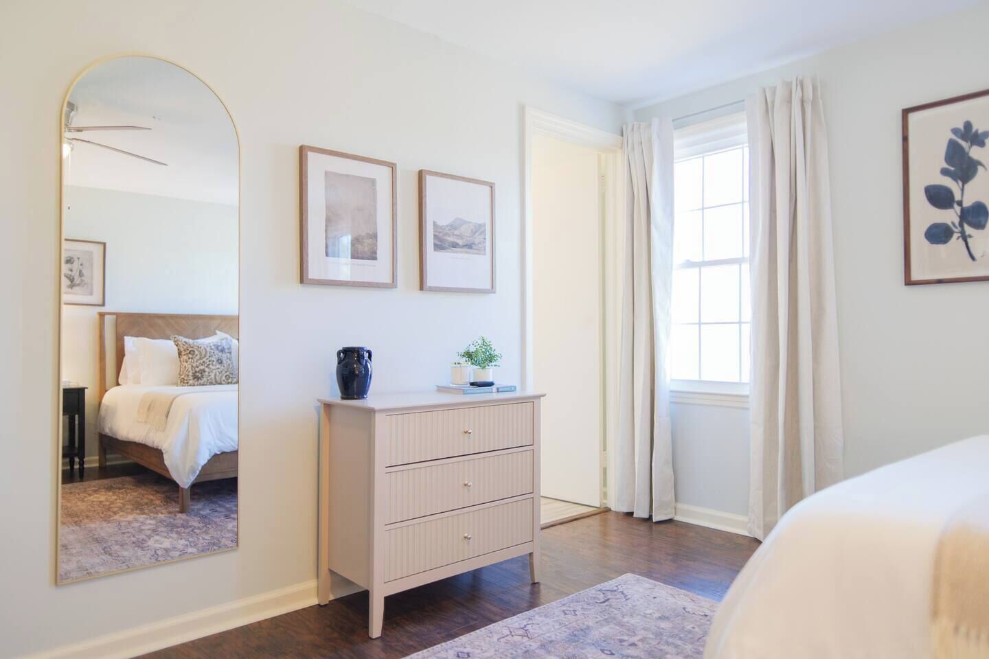 Une chambre à coucher avec un lit, une commode, un miroir et des tableaux encadrés accrochés au mur.