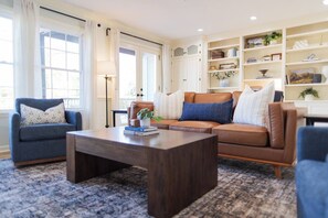 Ein Wohnzimmer mit braunem Ledersofa, einem blauen Sessel, einem Holztisch und einem gemusterten Teppich.