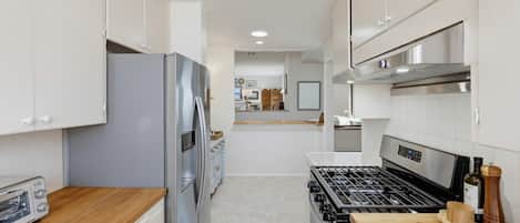 Una cocina moderna con armarios blancos, un refrigerador de acero inoxidable, una estufa a gas y una encimera de madera.