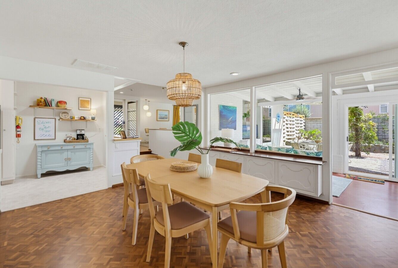 Un espace repas avec une table et des chaises en bois, un luminaire suspendu et une vue sur l’extérieur grâce à de grandes fenêtres.