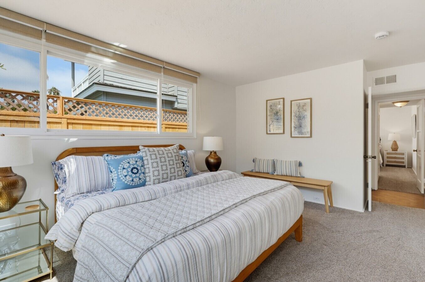 Une chambre à coucher avec un grand lit, des tables de chevet, un banc et une vue sur un balcon.