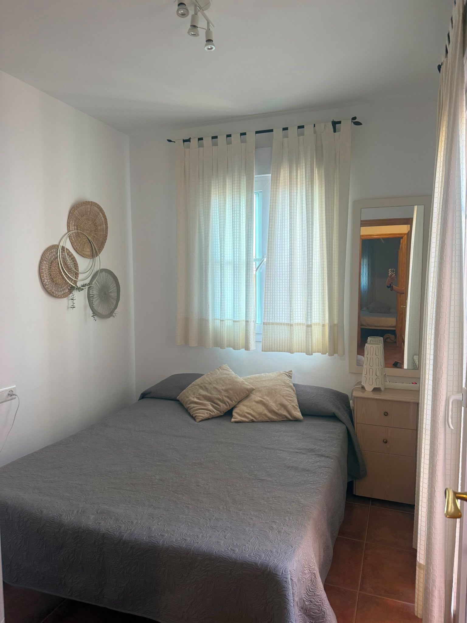 Une chambre à coucher avec un lit, une commode, un miroir et une fenêtre avec des rideaux.
