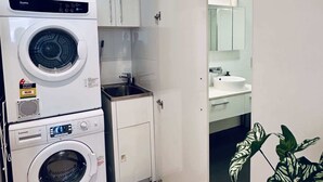 A compact laundry area with stacked washing machines, a small sink, and a cabinet. - Stylish 1-Bed Apartment in Adelaide CBD (Adelaide)