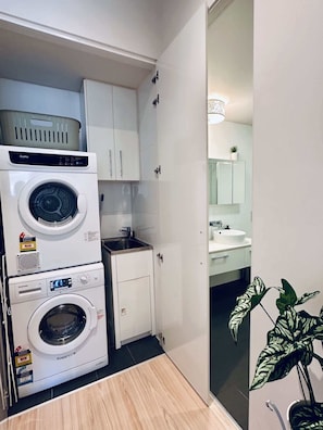 A compact laundry area with stacked washing machines, a small sink, and a cabinet. - Stylish 1-Bed Apartment in Adelaide CBD (Adelaide)
