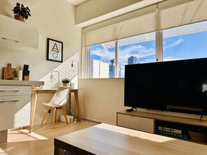 A modern living space with a large window, a flat-screen TV, a desk with a chair, and a kitchen area. - Stylish 1-Bed Apartment in Adelaide CBD (Adelaide)