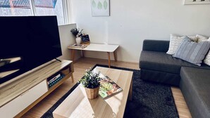A modern living room with a flat-screen TV, a coffee table with a plant, a grey sofa, and a small table with decorative items. - Stylish 1-Bed Apartment in Adelaide CBD (Adelaide)