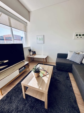 A modern living room with a flat-screen TV, a coffee table with a plant, a grey sofa, and a small table with decorative items. - Stylish 1-Bed Apartment in Adelaide CBD (Adelaide)