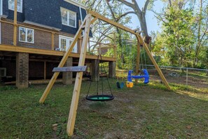 A wooden swing set in a backyard with a brick house in the background. - Sleeps 18 Riverfront Getaway with Game Room & Deck (Valdosta)