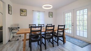 A dining area with a wooden table, four chairs, a high ceiling with a circular light fixture, and a view through large windows. - Sleeps 18 Riverfront Getaway with Game Room & Deck (Valdosta)