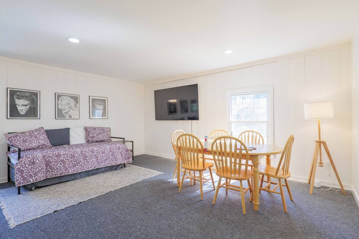 A room with a sofa, a dining table with chairs, a flat-screen TV, and a lamp.