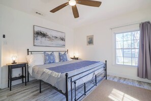 Une chambre à coucher avec un lit, deux tables de chevet, un ventilateur de plafond et une fenêtre avec des rideaux.
