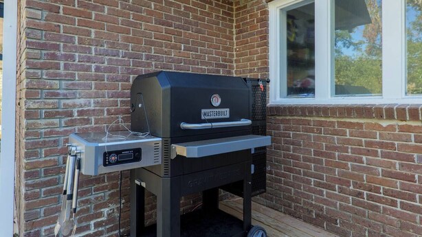 A gas-powered barbecue grill with a digital display, positioned against a brick wall with a window above it. - Sleeps 18 Riverfront Getaway with Game Room & Deck (Valdosta)