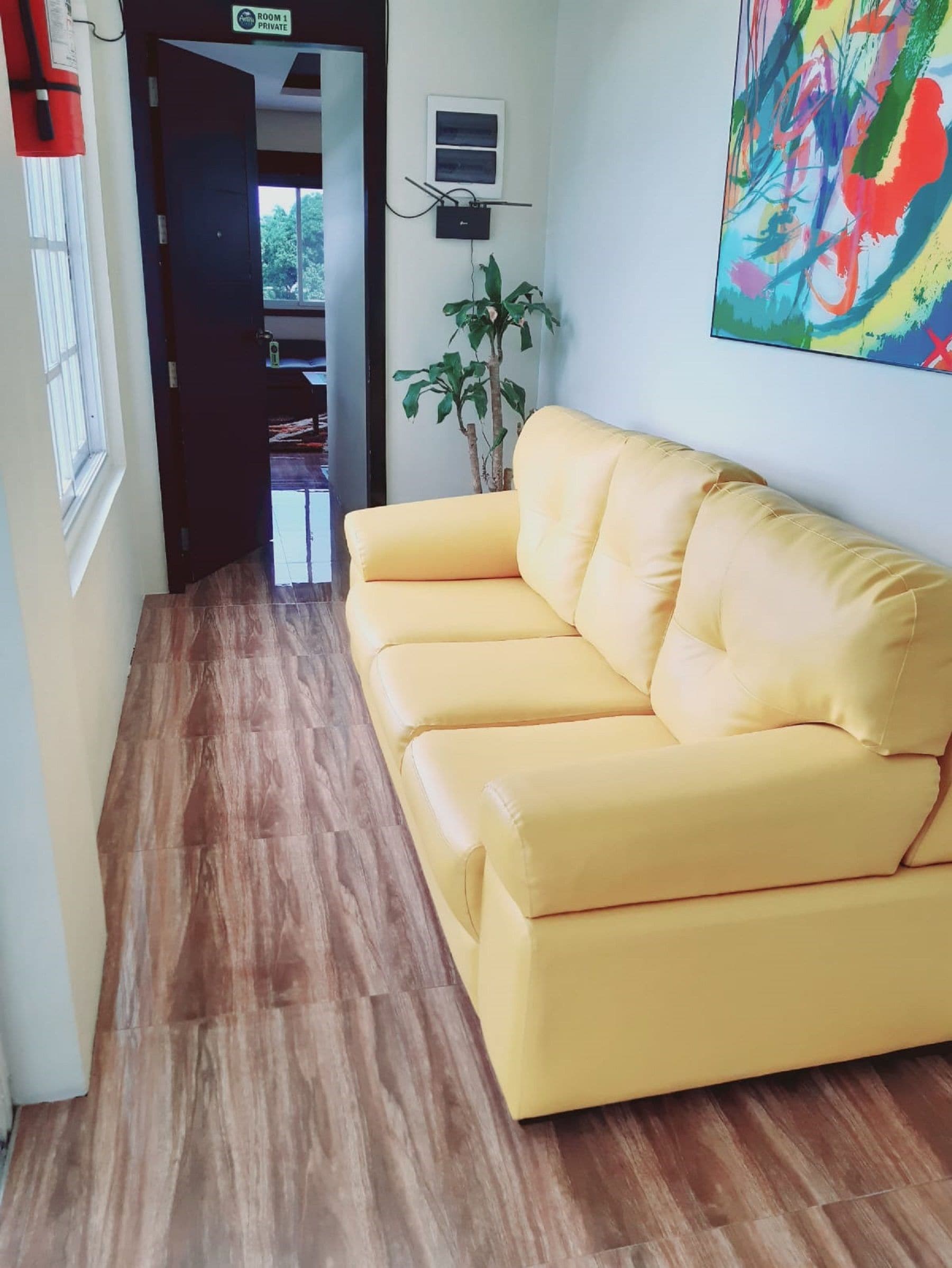 Ein gelbes Sofa in einer Diele mit Holzboden, einem Blumentopf und einem farbenfrohen abstrakten Gemälde an der Wand.