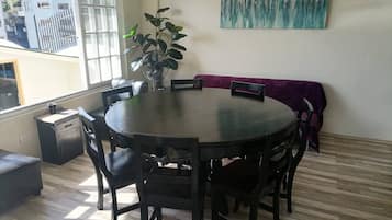 A dining area with a round table, six chairs, a purple sofa, a potted plant, and a painting on the wall.
