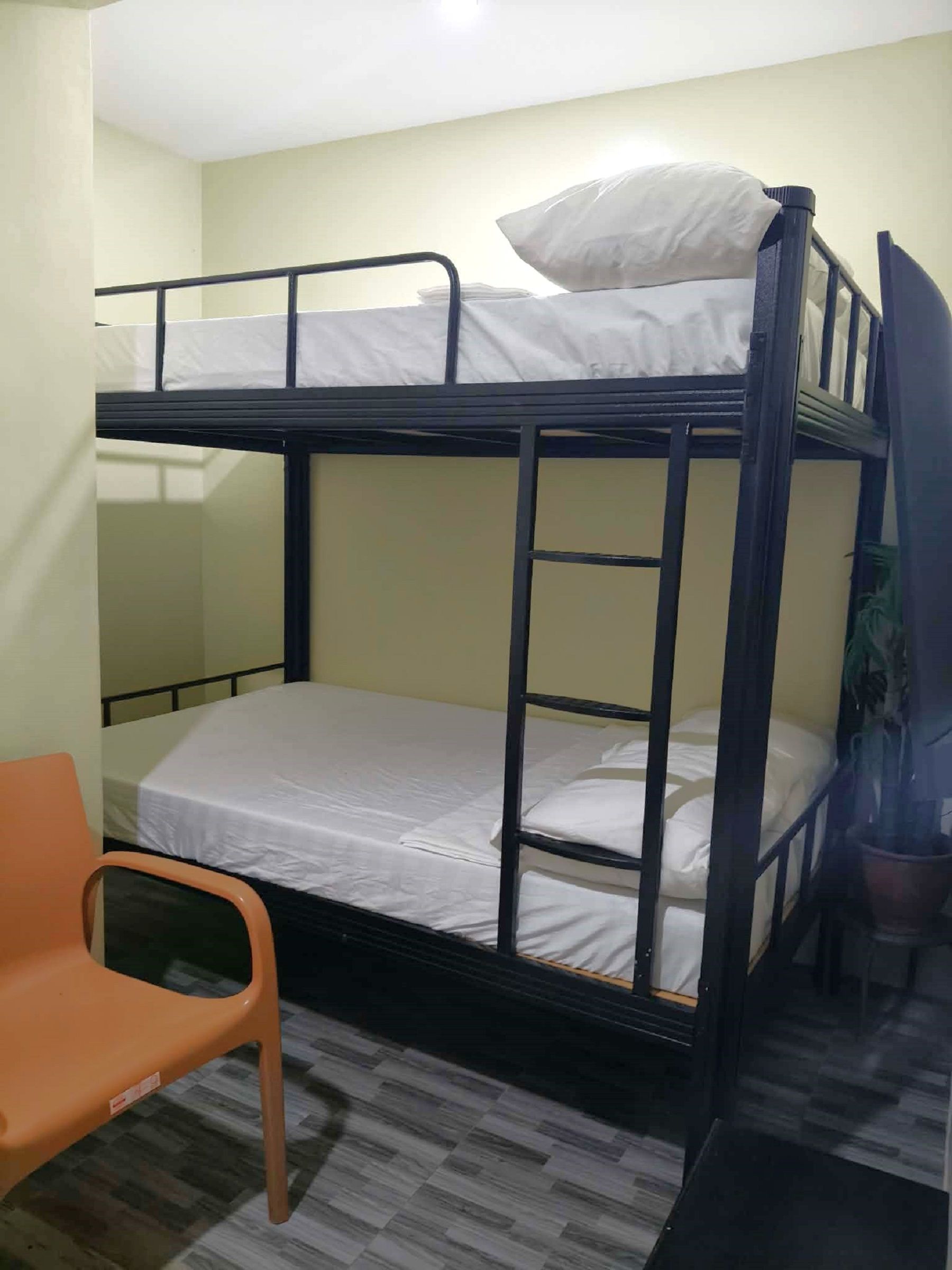 A bunk bed with a mattress and pillows, a plastic chair, and a potted plant.
