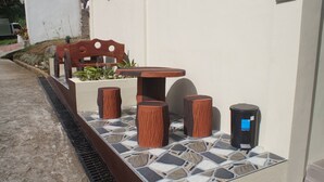 An outdoor seating area with a table and stools, a trash bin, and a planter with plants.