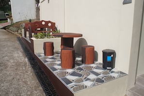 Zona exterior amb seients, una taula, tamborets, un safataire i una jardineria amb plantes.