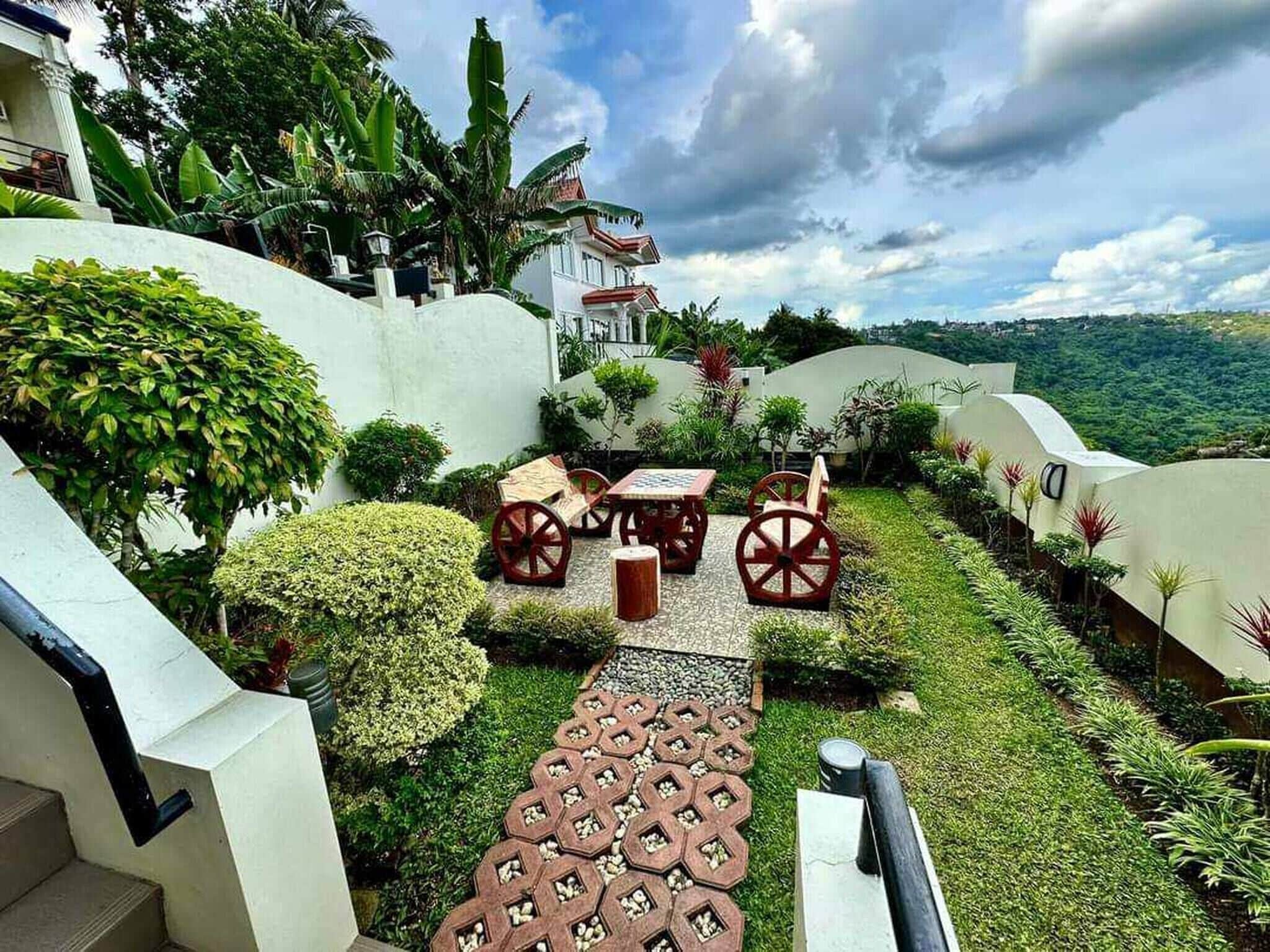 A garden with a paved walkway, seating area, and a view of a hill.