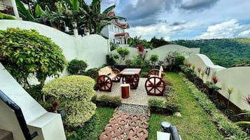 A garden with a paved walkway, seating area, and a view of a hill.
