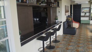 A kitchen with a black countertop and three bar stools. There is a dining area with a red chair and a green bench. The floor has a patterned tile design.