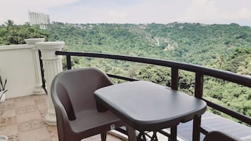 A balcony with a table and chairs, overlooking a lush green landscape with a building in the distance.