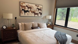 A bedroom with a large bed, two bedside tables, a clock, a framed artwork, and a window with a view of trees. - My Place in Powder House Pass, Paved Roads, AC, Hot Tub! (Lead)