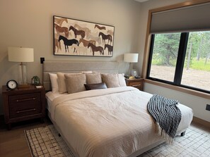 A bedroom with a large bed, two bedside tables, a clock, a framed artwork, and a window with a view of trees. - My Place in Powder House Pass, Paved Roads, AC, Hot Tub! (Lead)