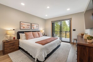 Une chambre à coucher avec un lit, des tables de chevet, une lampe, une fenêtre donnant sur un beau paysage et un téléviseur.