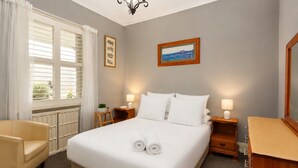 A hotel room with a large bed, two bedside tables with lamps, a chair, a window with curtains, and a framed picture on the wall. - Tranquil Cottage Lovely Street, Walk to Leura (Leura)