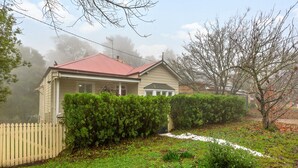 A residential house with a red roof, surrounded by a white picket fence, dense green shrubbery, and a clear path leading to the front door. - Tranquil Cottage Lovely Street, Walk to Leura (Leura)