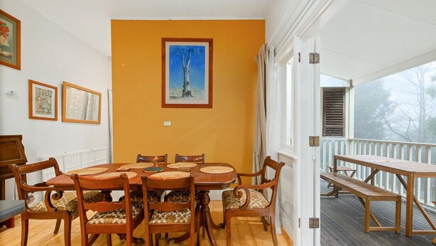 A dining area with a wooden table and chairs, a framed painting on the wall, and a view of the outdoors through a door. - Tranquil Cottage Lovely Street, Walk to Leura (Leura)