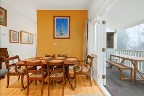 Zona de dinar amb taula i cadires de fusta, un quadre amb marc a la paret i vistes a l'exterior a través d'una porta.