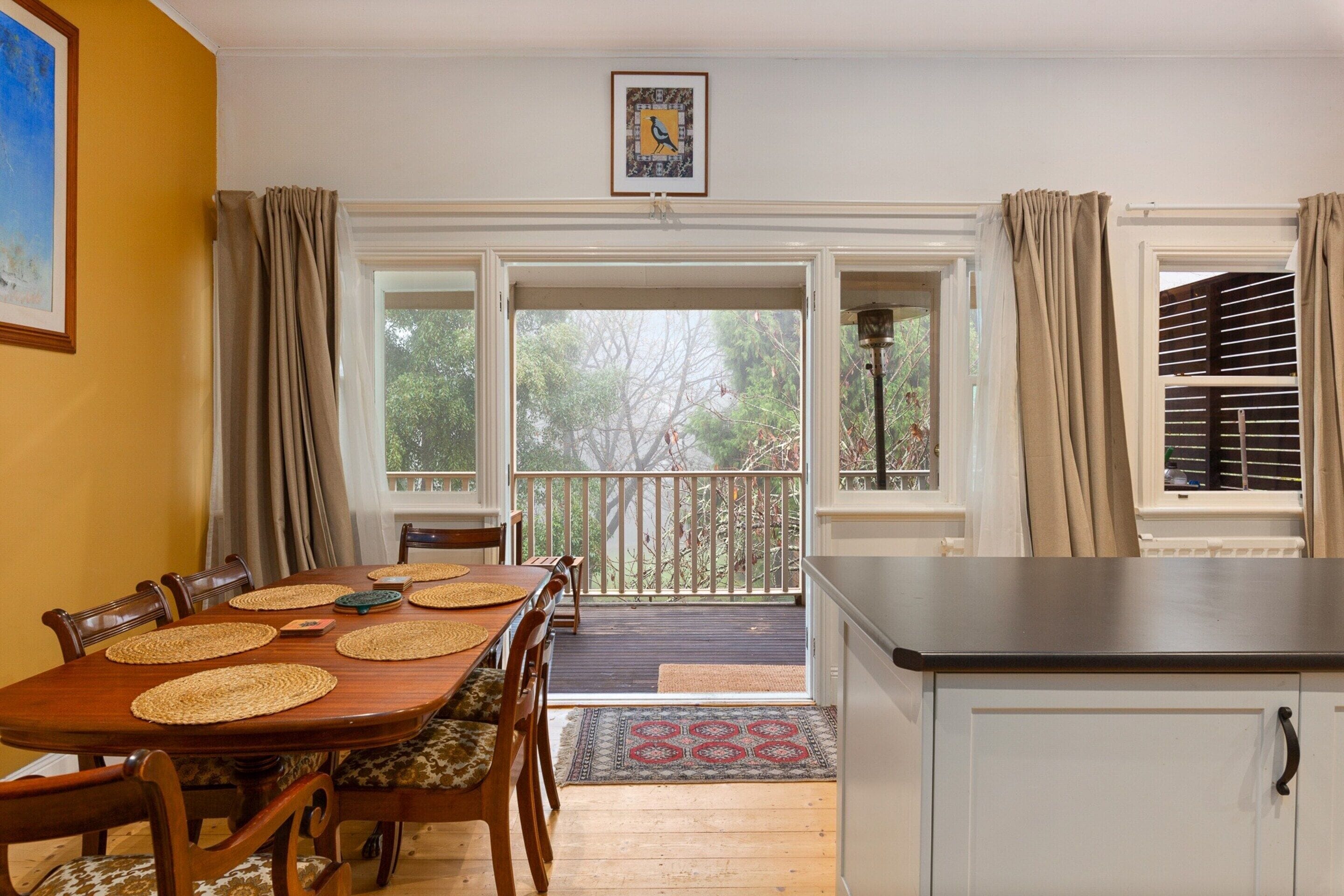 A dining area with a wooden table and chairs, a kitchen area with a countertop, and a view of the outdoors through a sliding glass door.