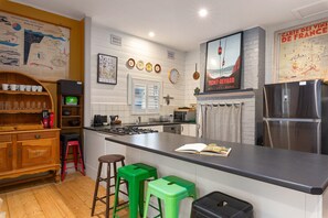 Una cuina moderna amb una illa central, tamborets de bar, un frigorífic i diversos electrodomèstics.