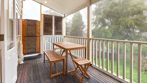 A covered outdoor area with a wooden table and benches, a view of trees through the railing, and a door with shutters. - Tranquil Cottage Lovely Street, Walk to Leura (Leura)