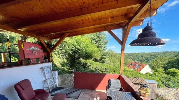 An outdoor patio with wooden furniture, a hanging light fixture, and a view of a house in the background. - Tuscan flair in the west of Dresden, not far from Nice in Saxony - Radebeul (Dresden)