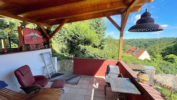 Eine Außenpatio mit Holzmöbeln, einer hängenden Lampe und Blick auf ein Haus im Hintergrund.