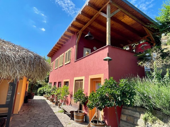 A red building with a wooden balcony, potted plants, and a thatched roof structure.