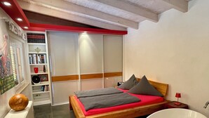 A modern bedroom with a wooden bed, a large bathtub, and a red accent wall. - Tuscan flair in the west of Dresden, not far from Nice in Saxony - Radebeul (Dresden)