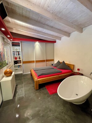 Ein modernes Schlafzimmer mit einem hölzernen Bett, einer großen Badewanne und einer roten Akzentwand.